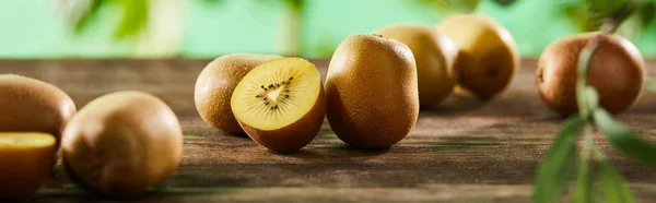 Panoramic shot of cut and whole kiwi on wooden surface — Stock Photo