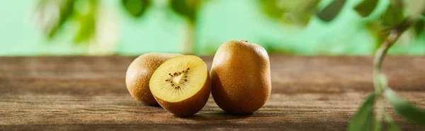Panoramic shot of cut and whole kiwi on wooden surface — Stock Photo