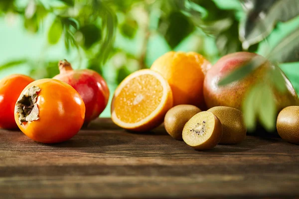 Selective focus of kiwi, oranges, pomegranate, mango and persimmons on wooden table — Stock Photo
