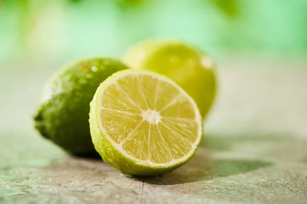 Selective focus of whole and cut limes with drops on marble surface — Stock Photo