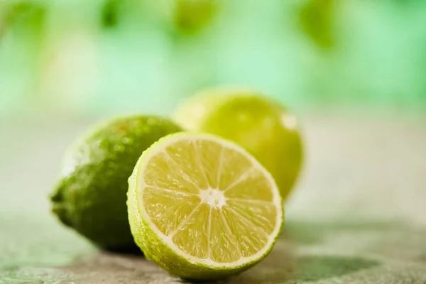 Selective focus of whole and cut limes with drops on marble surface — Stock Photo