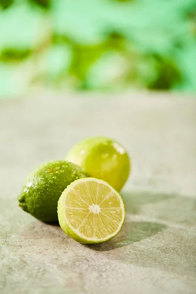 Enfoque selectivo de limas enteras y cortadas con gotas en la superficie de mármol - foto de stock