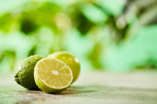 Enfoque selectivo de limas enteras y cortadas con gotas en la superficie de mármol - foto de stock