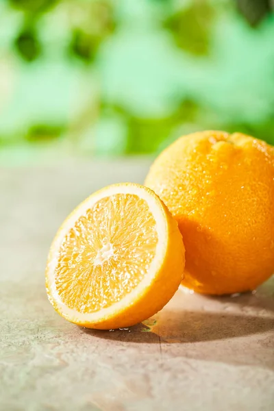 Selective focus of cut and whole oranges with drops on marble surface — Stock Photo