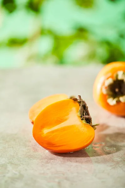 Selective focus of whole and cut persimmons on marble surface — Stock Photo