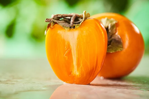 Selective focus of whole and cut persimmons on marble surface — Stock Photo