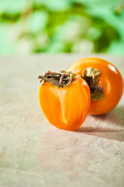 Selective focus of whole and cut persimmons on marble surface — Stock Photo