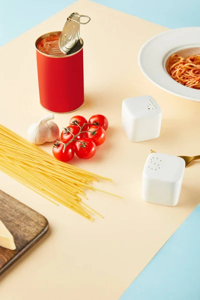 Deliziosi spaghetti con salsa di pomodoro in piatto vicino agli ingredienti su fondo blu e giallo — Foto stock