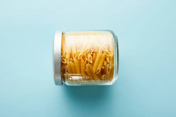 Top view of raw penne in jar on blue background with copy space — Stock Photo