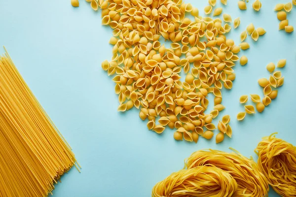 Draufsicht auf rohe Conchiglie, Linguini und Spaghetti auf blauem Hintergrund — Stockfoto