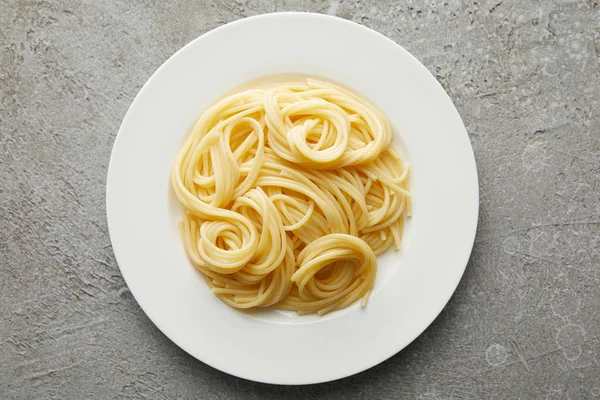 Vista dall'alto di deliziosi spaghetti su piatto su superficie grigia testurizzata — Foto stock