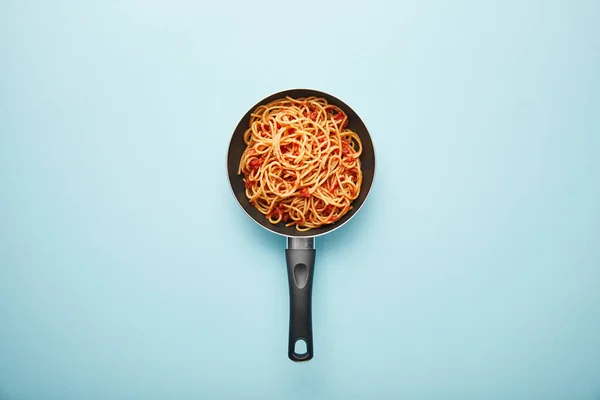 Вид сверху на вкусные спагетти с томатным соусом в сковороде на голубом фоне — стоковое фото