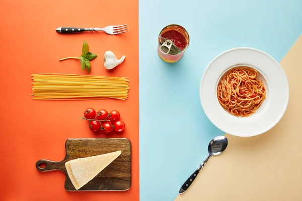 Flat lay with delicious spaghetti with tomato sauce in plate near cutlery and ingredients on blue, red and yellow background — Stock Photo