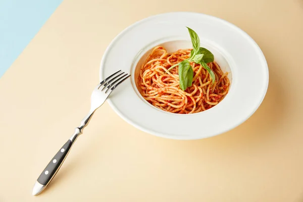 Спагетті з томатним соусом в тарілці біля виделки на синьо-жовтому фоні — стокове фото