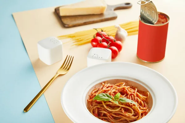 Foco seletivo de espaguete delicioso com molho de tomate na placa perto de garfo no fundo azul e amarelo — Fotografia de Stock