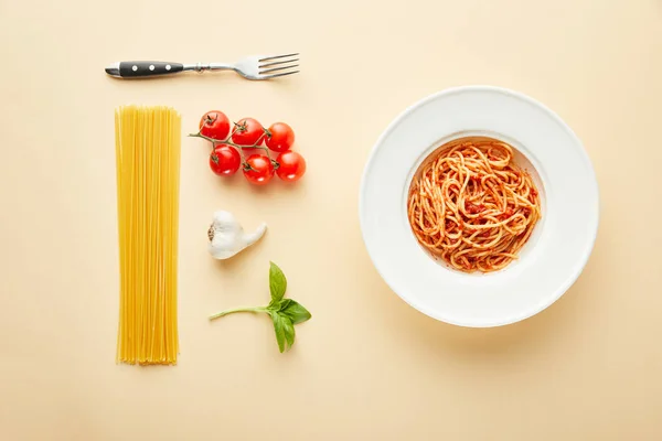 Flat lay com delicioso espaguete com molho de tomate em prato perto de garfo e ingredientes em fundo amarelo — Fotografia de Stock