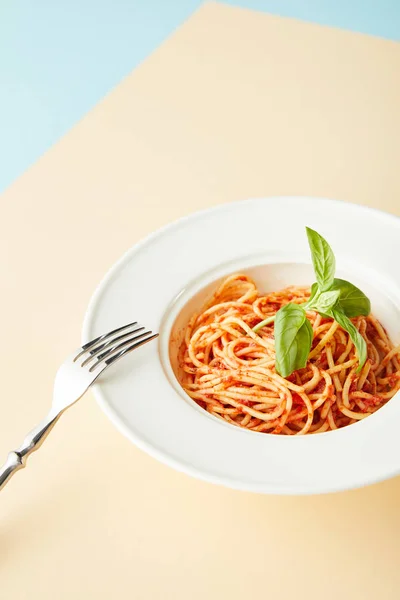 Вкусные спагетти с томатным соусом в тарелке рядом с вилкой на синем и желтом фоне — стоковое фото