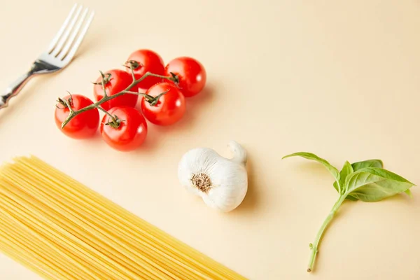 Rohe Spaghetti, Knoblauch, Tomaten, Basilikum und Gabel auf gelbem Hintergrund — Stockfoto