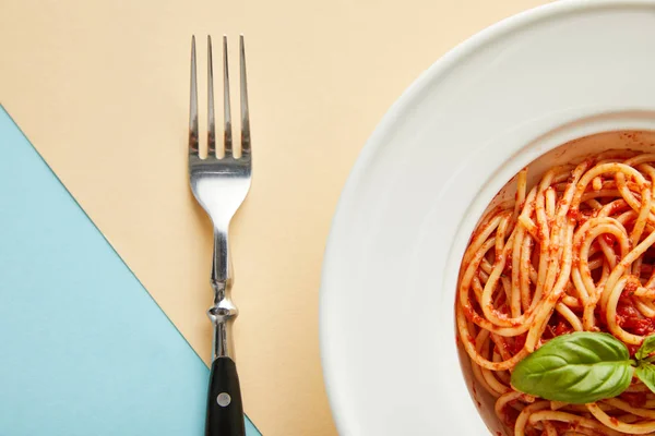 Vista dall'alto di deliziosi spaghetti con salsa di pomodoro in piatto vicino alla forchetta su sfondo blu e giallo — Foto stock