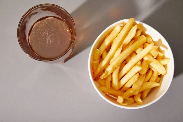 Vista superior de cerveja em vidro perto de deliciosas batatas fritas em balde no fundo cinza — Fotografia de Stock