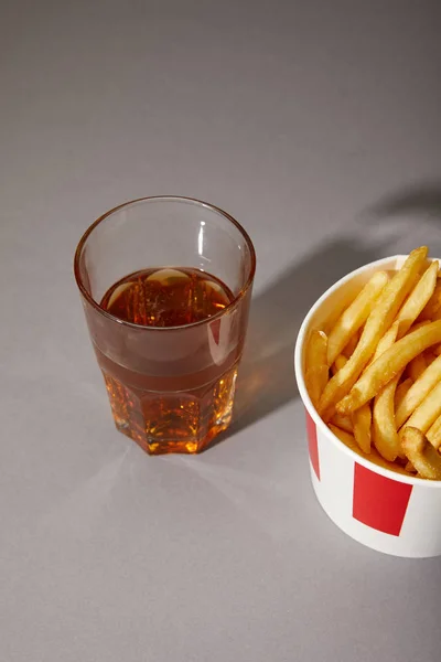 Cerveza en vaso cerca de deliciosas papas fritas en cubo sobre fondo gris - foto de stock