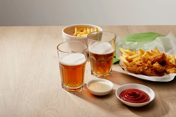 Verres de bière, pépites de poulet avec frites, ketchup et mayonnaise sur table en bois sur fond gris — Photo de stock