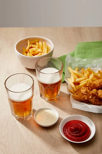 Biergläser, Chicken Nuggets mit Pommes, Ketchup und Mayonnaise auf Holztisch vor grauem Hintergrund — Stockfoto