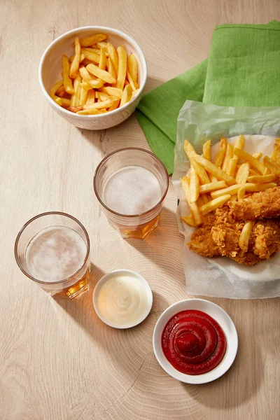 Vista superior de copos de cerveja, nuggets de frango com batatas fritas, ketchup e maionese na mesa de madeira — Fotografia de Stock