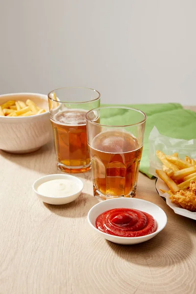 Glasses of beer, chicken nuggets with french fries, ketchup and mayonnaise on wooden table on grey background — Stock Photo