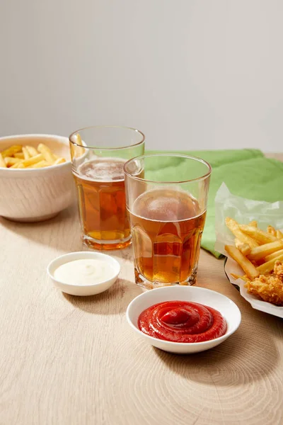 Biergläser, Chicken Nuggets mit Pommes, Ketchup und Mayonnaise auf Holztisch vor grauem Hintergrund — Stockfoto