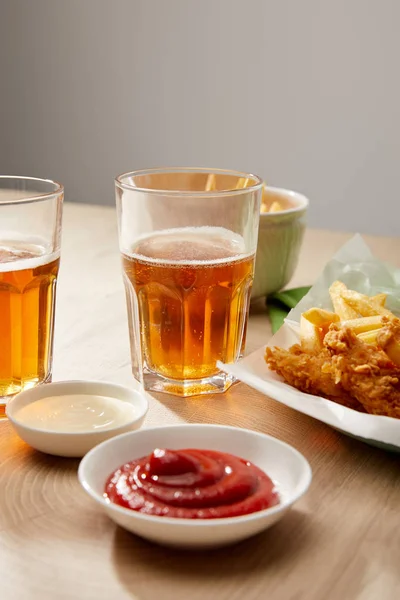 Biergläser, Chicken Nuggets mit Pommes, Ketchup und Mayonnaise auf Holztisch vor grauem Hintergrund — Stockfoto