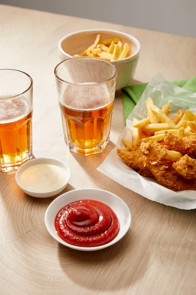 Bicchieri di birra, pepite di pollo con patatine fritte, ketchup e maionese su tavolo di legno su sfondo grigio — Foto stock