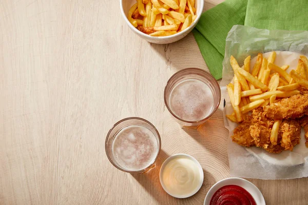 Vista superior de copos de cerveja, nuggets de frango com batatas fritas, ketchup e maionese em mesa de madeira com espaço de cópia — Fotografia de Stock