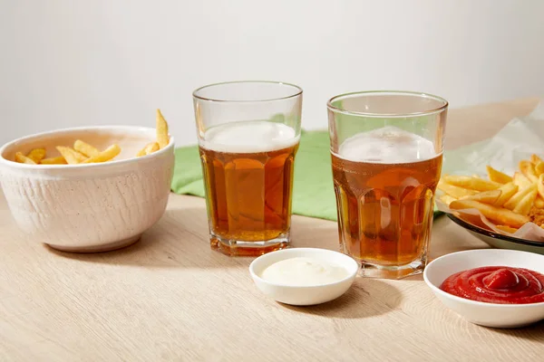 Бокалы пива, куриные наггетсы с картошкой фри, кетчуп и майонез на деревянном столе на сером фоне — стоковое фото