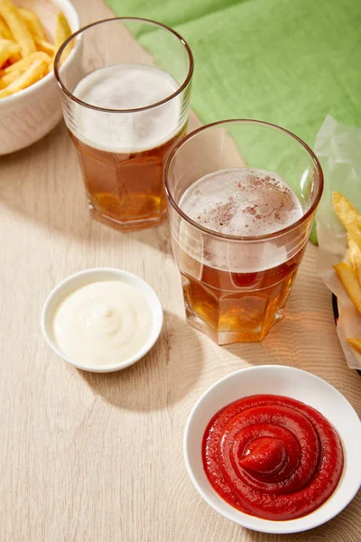 Copos de cerveja, batatas fritas, ketchup e maionese em mesa de madeira em fundo cinza — Fotografia de Stock