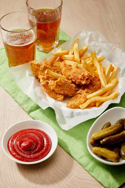 Verres de bière, pépites de poulet avec frites, sauces et cornichons sur table en bois — Photo de stock