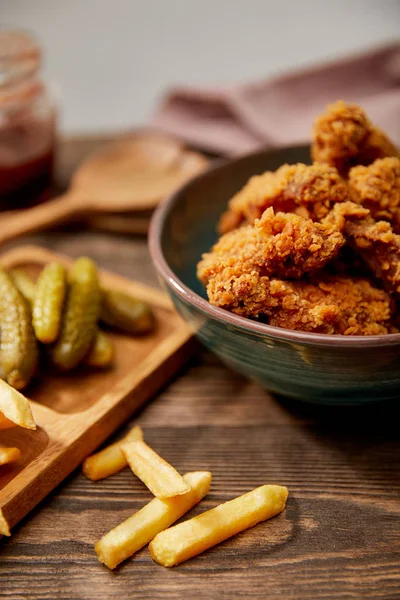 Foyer sélectif de délicieuses pépites de poulet, frites et cornichons sur table en bois — Photo de stock