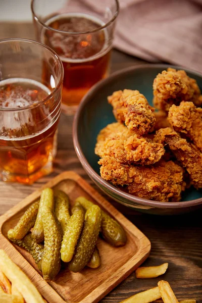 Deliziose pepite di pollo, patatine fritte e cetriolini vicino a bicchieri di birra sul tavolo di legno — Foto stock