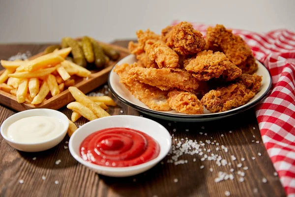 Leckere Chicken Nuggets, Ketchup, Mayonnaise, Pommes und Gurken auf Holztisch mit Salz und rustikaler karierter Serviette isoliert auf grau — Stockfoto