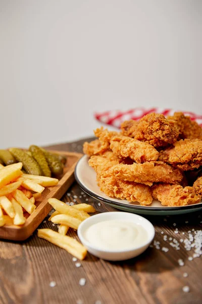 Selective focus of delicious chicken nuggets, mayonnaise, french fries and gherkins on wooden table with salt and rustic plaid napkin isolated on grey — Stock Photo