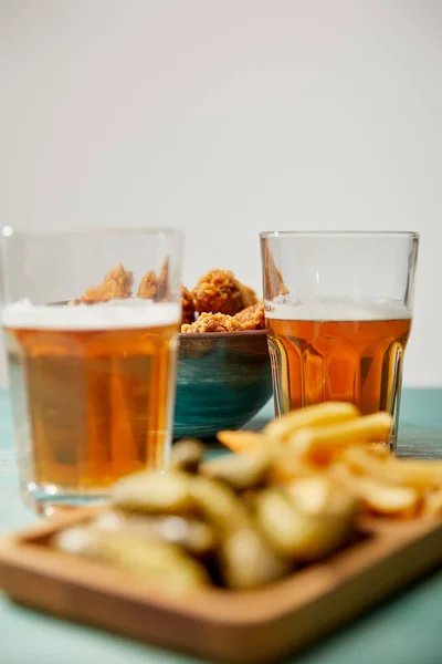 Foco seletivo de deliciosas pepitas de frango, batatas fritas e pepinos perto de copos de cerveja em mesa de madeira turquesa em fundo cinza — Fotografia de Stock