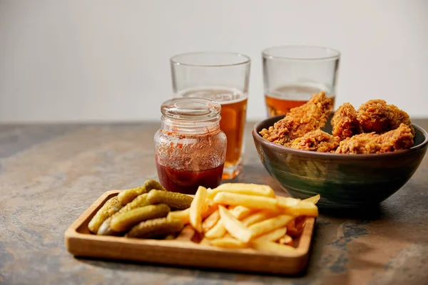 Delicioso pollo nuggets, papas fritas y pepinillos cerca de vasos de cerveza en la superficie de piedra aislado en gris - foto de stock