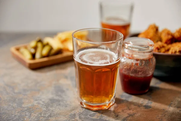 Selective focus of delicious chicken nuggets, sauce, french fries and gherkins near glasses of beer on stone surface isolated on grey — Stock Photo