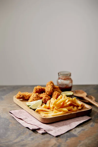 Wooden board with delicious chicken nuggets, french fries and lime on stone surface isolated on grey — Stock Photo