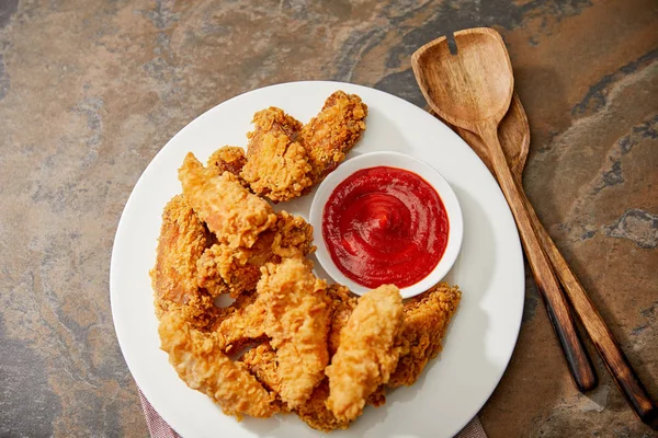 Vista superior de deliciosas pepitas de pollo con salsa de tomate y espátulas de madera en la superficie de piedra - foto de stock