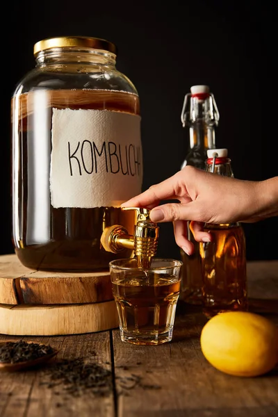 Vue recadrée de la femme versant kombucha dans le verre de bocal sur table en bois isolé sur noir — Photo de stock