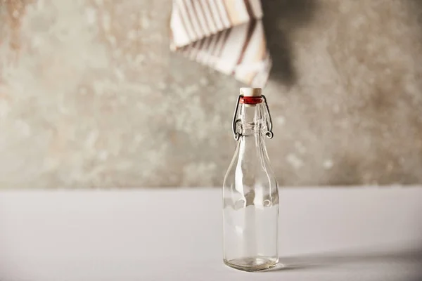 Selective focus of empty glass bottle near striped napkin on stone wall — Stock Photo