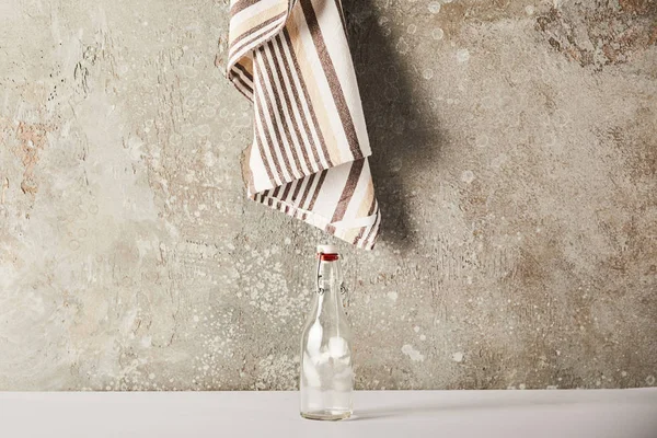 Leere Glasflasche neben gestreifter Serviette auf Steinwand — Stockfoto