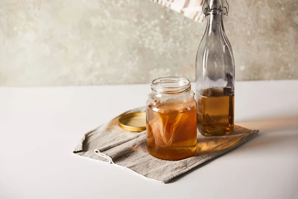 Glas mit Kombucha nahe Flasche auf grauer Serviette auf weißem Tisch — Stockfoto