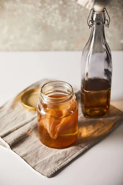 Jar with kombucha near bottle on grey napkin on white table — Stock Photo